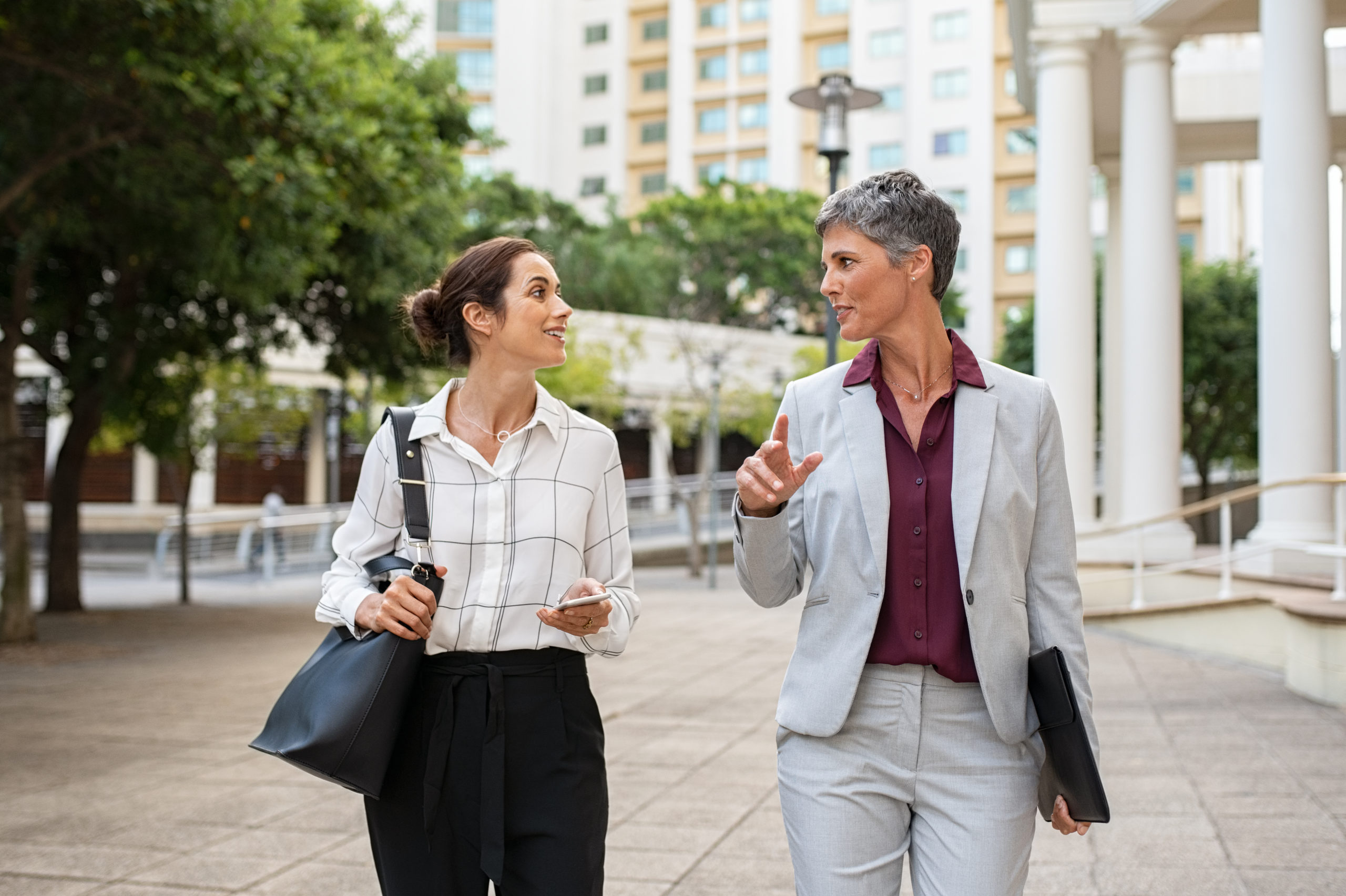Two business women in conversation walking on city street. Corpo